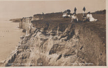 Load image into Gallery viewer, Vintage photograph of people sitting on a cliff edge with a beach in the background