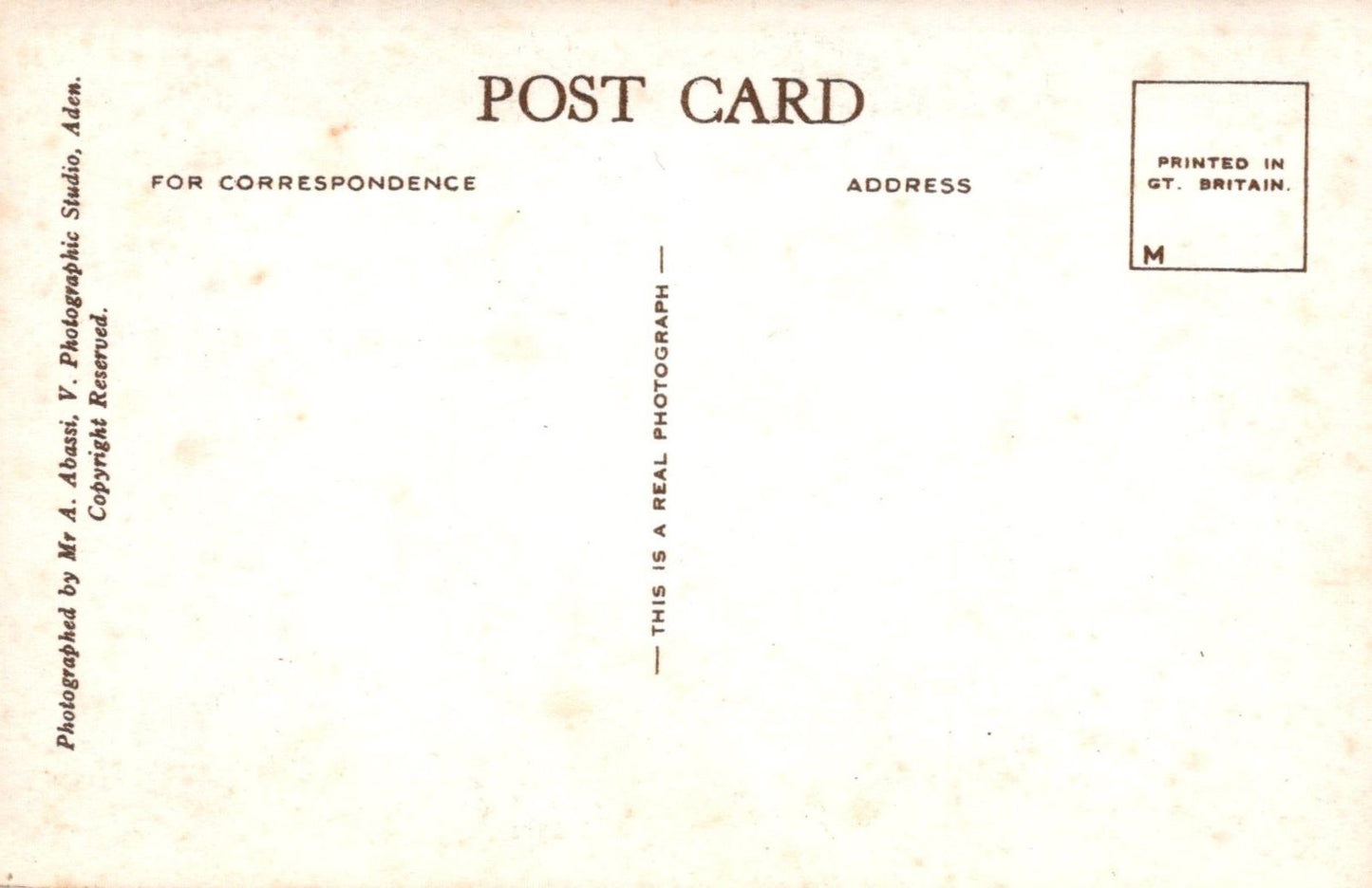 Back of a postcard with text and a small square logo on a beige background