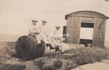 Load image into Gallery viewer, Vintage black and white photo of three men sitting on a large cylindrical object with a corrugated metal shed in the background.