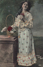 Load image into Gallery viewer, Woman in a floral dress holding flowers and a basket, with a dark background