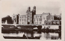Load image into Gallery viewer, Historic black and white photo of a large building with a river and boat in front