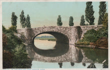 Load image into Gallery viewer, Stone bridge over a body of water with trees on either side, vintage style.