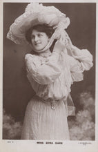 Load image into Gallery viewer, Vintage black and white photograph of a woman in an elaborate dress and hat, with a blurred background.