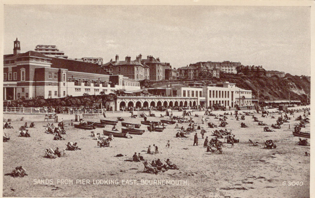 Vintage black and white photo of a beach scene with buildings and people from a pier in Bournemouth.