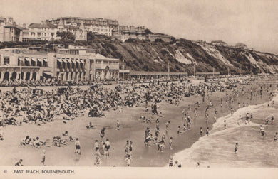Vintage black and white photo of a crowded beach with buildings in the background