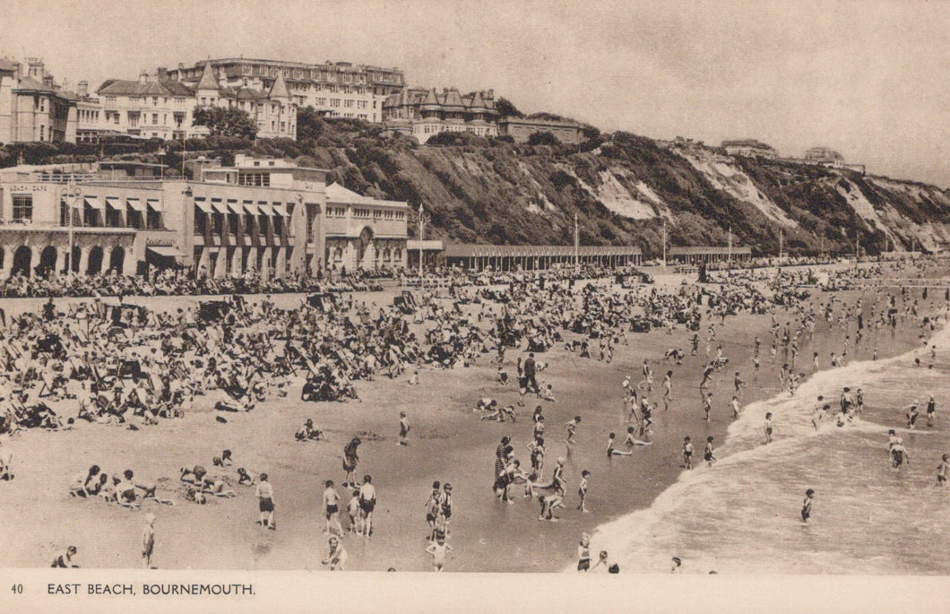 Vintage black and white photo of a crowded beach with buildings in the background