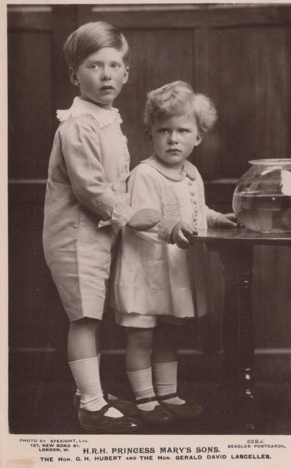 Two young boys standing next to a fishbowl in a vintage black and white photograph.