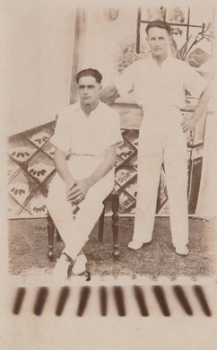 Two men in cricket uniforms standing outdoors with a decorative background