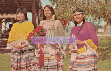 Three women in traditional attire standing outdoors with a 'Mo's Postcards' logo overlay.