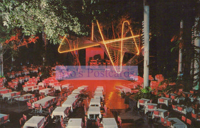 Outdoor event with tables and chairs under a large illuminated sign at night.