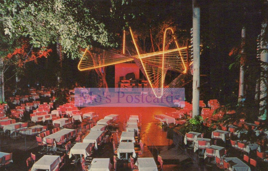 Outdoor event with tables and chairs under a large illuminated sign at night.