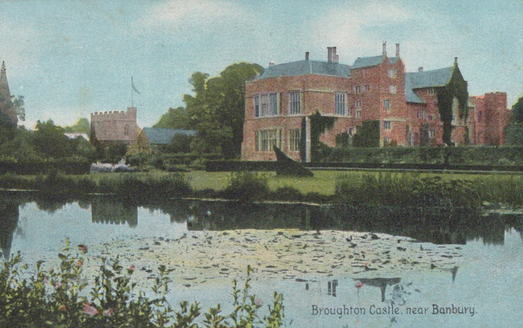 Historic brick building with a moat, likely a castle, in a scenic setting.