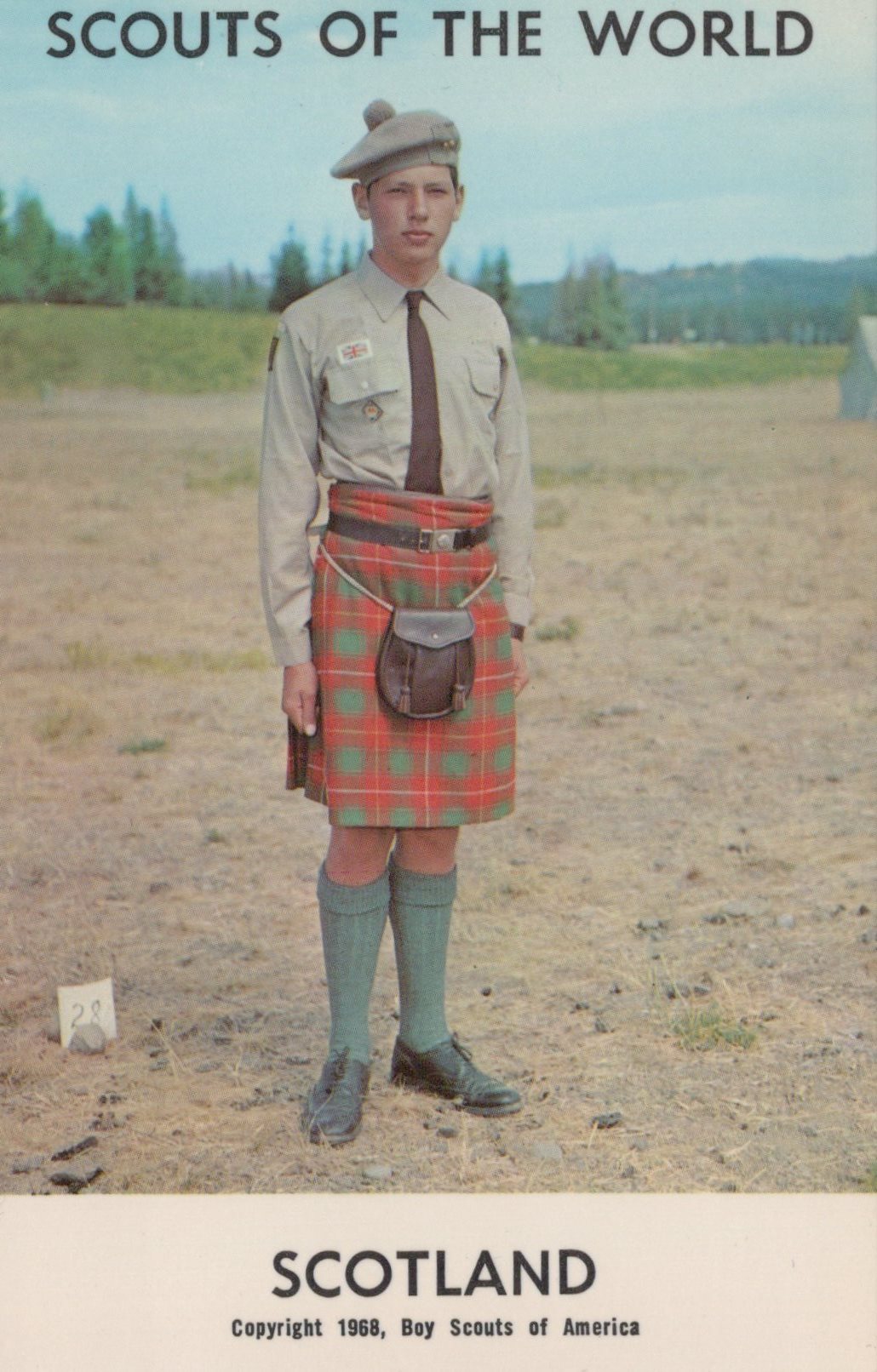 Scout in uniform with a kilt standing outdoors, with 'Scouts of the World' and 'Scotland' text at the top.