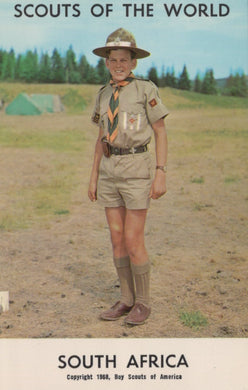 Scout in uniform standing outdoors with trees and tents in the background, labeled 'Scouts of the World, South Africa'.