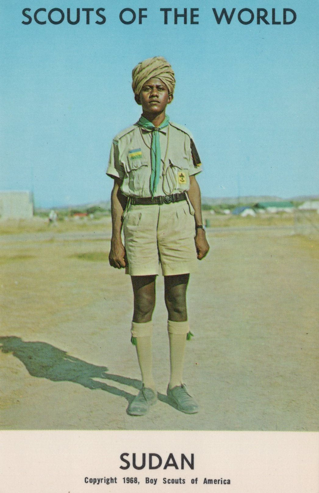 Scout in uniform with a turban standing on a road, with text 'Scouts of the World Sudan' at the bottom.