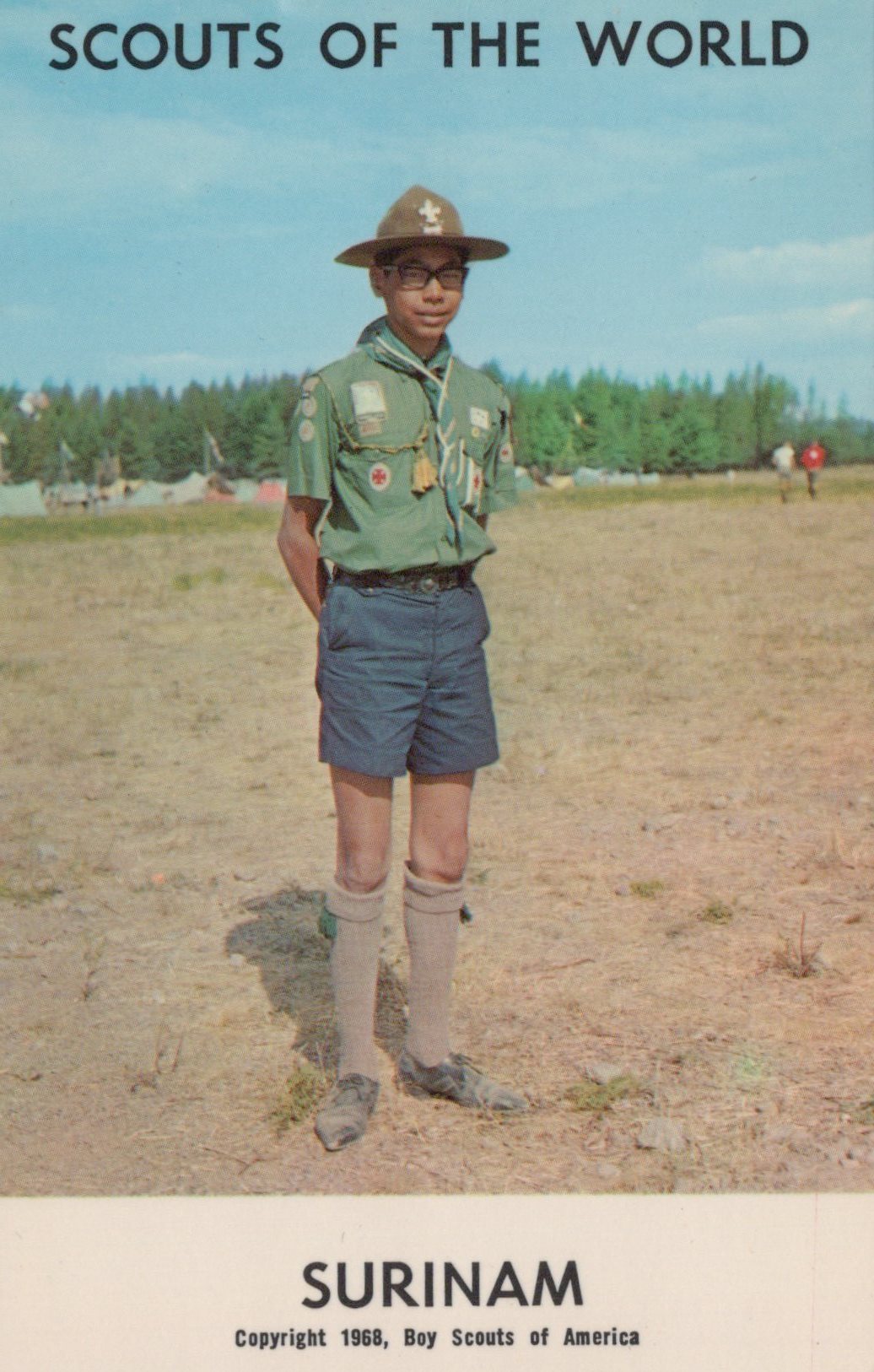 Scout in Surinam wearing a green uniform with a hat, standing in an open field.