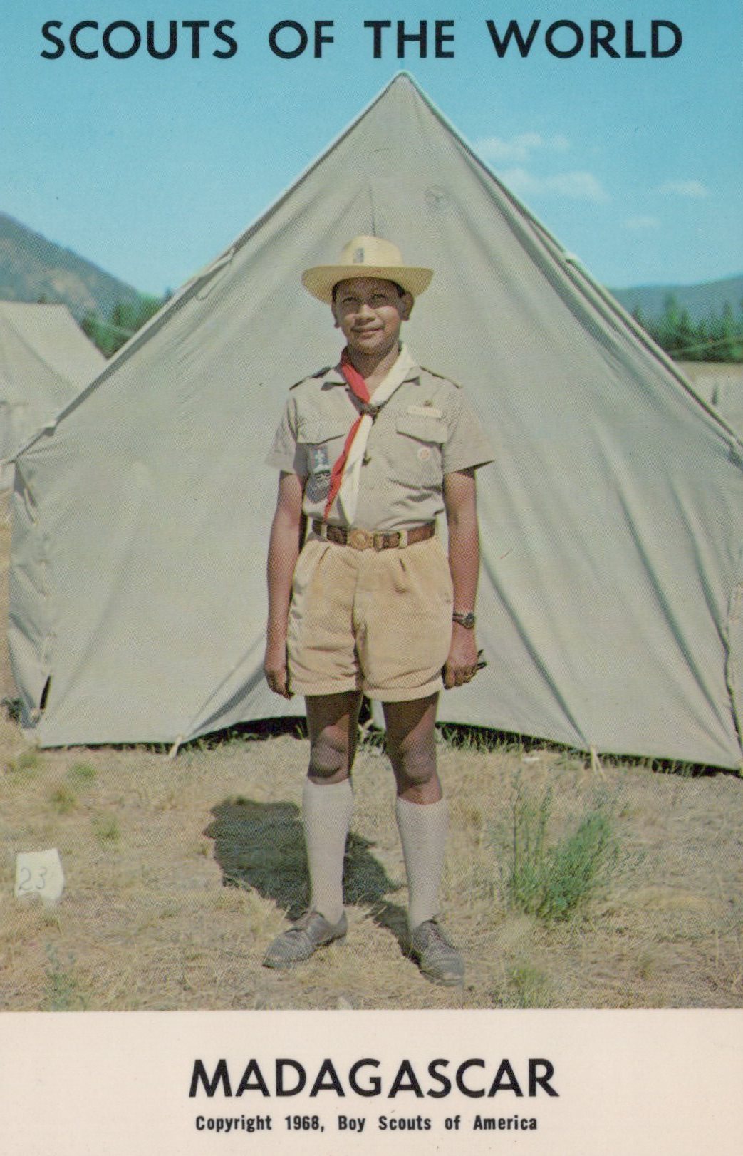 Scout in uniform standing in front of a tent with 'Scouts of the World' and 'Madagascar' text.