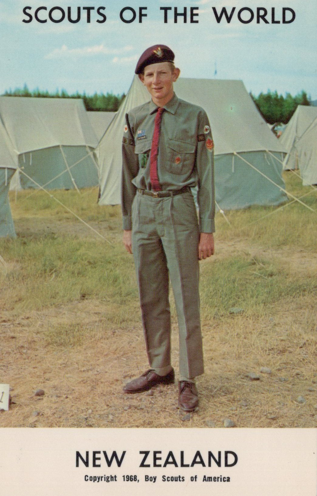 Scout in uniform standing in front of tents with 'Scouts of the World' and 'New Zealand' text.