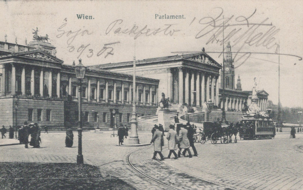 Vintage black and white photo of a city street with people and horse-drawn carriages, featuring architectural buildings.