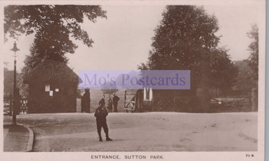 Vintage black and white photo of a person standing in front of a gate at Sutton Park, with 'Mo's Postcards' watermark.