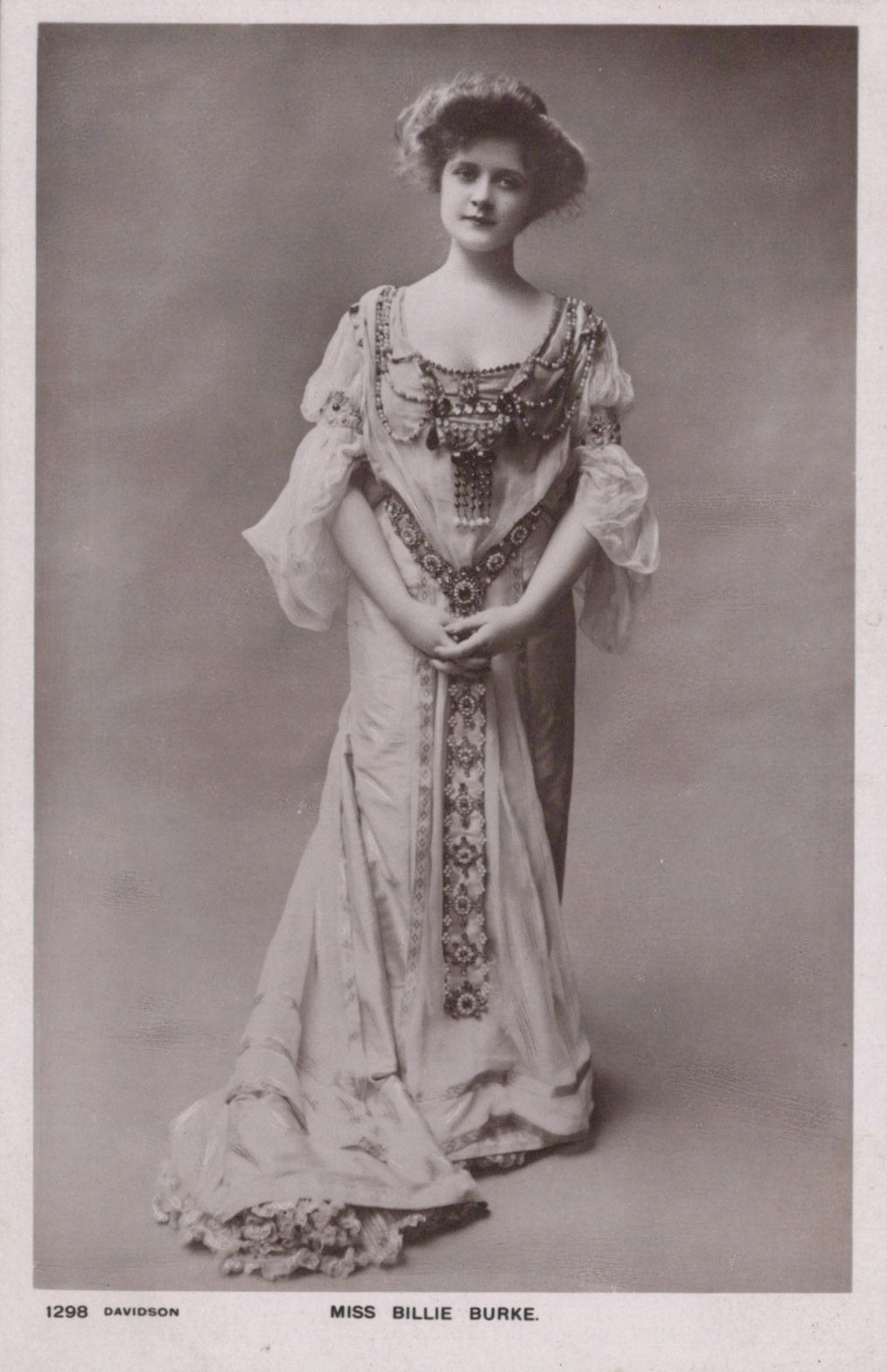 Vintage black and white photograph of a woman in an ornate dress against a plain background