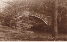 Load image into Gallery viewer, Vintage photograph of a stone bridge over a stream with trees on either side.
