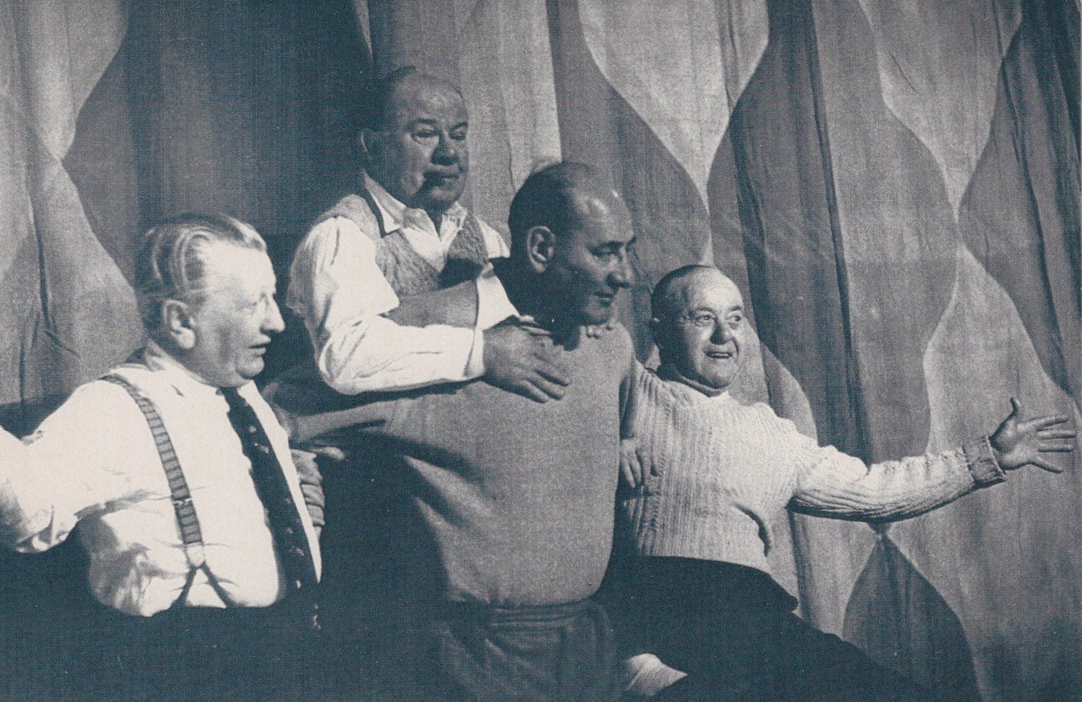 Black and white photograph of four men posing together against a curtain backdrop