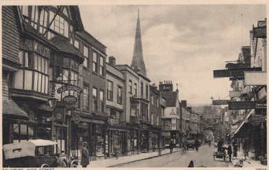 Vintage black and white photo of a street scene with shops and a church spire.