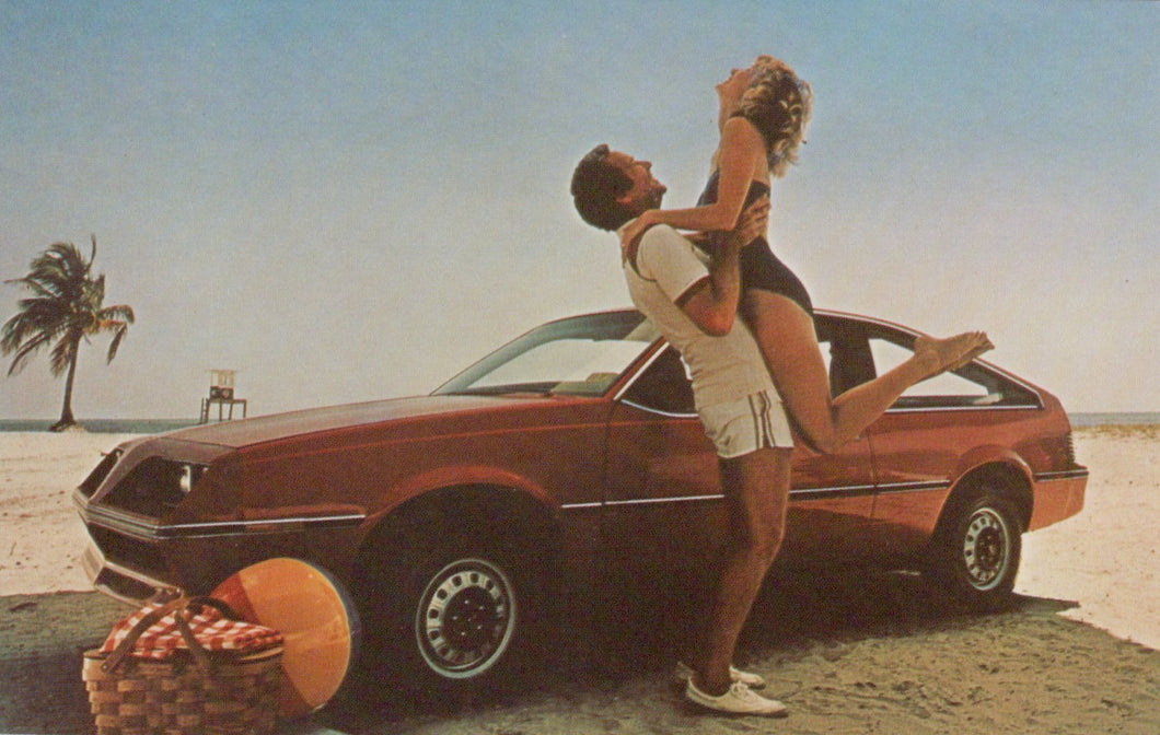 Man lifting a woman in front of a red car on a beach