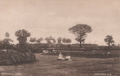 Vintage black and white photograph of a park scene with people sitting on a bench, trees, and a gazebo.