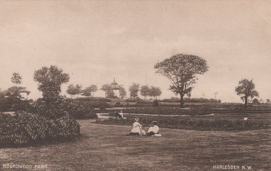 Vintage black and white photograph of a park scene with people sitting on a bench, trees, and a gazebo.