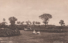 Load image into Gallery viewer, Vintage black and white photograph of a park scene with people sitting on a bench, trees, and a gazebo.
