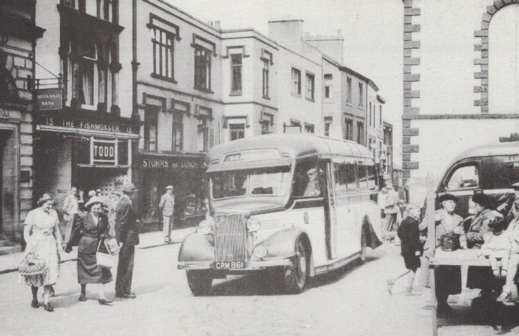Vintage black and white photo of a bus on a city street with people and buildings in the background.