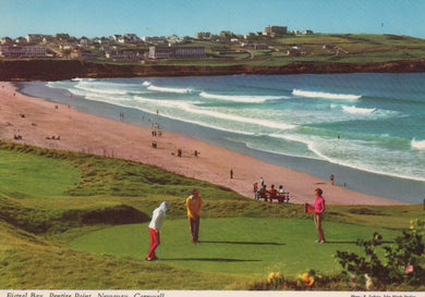 People playing golf on a grassy area near a beach with waves and a coastal town in the background.