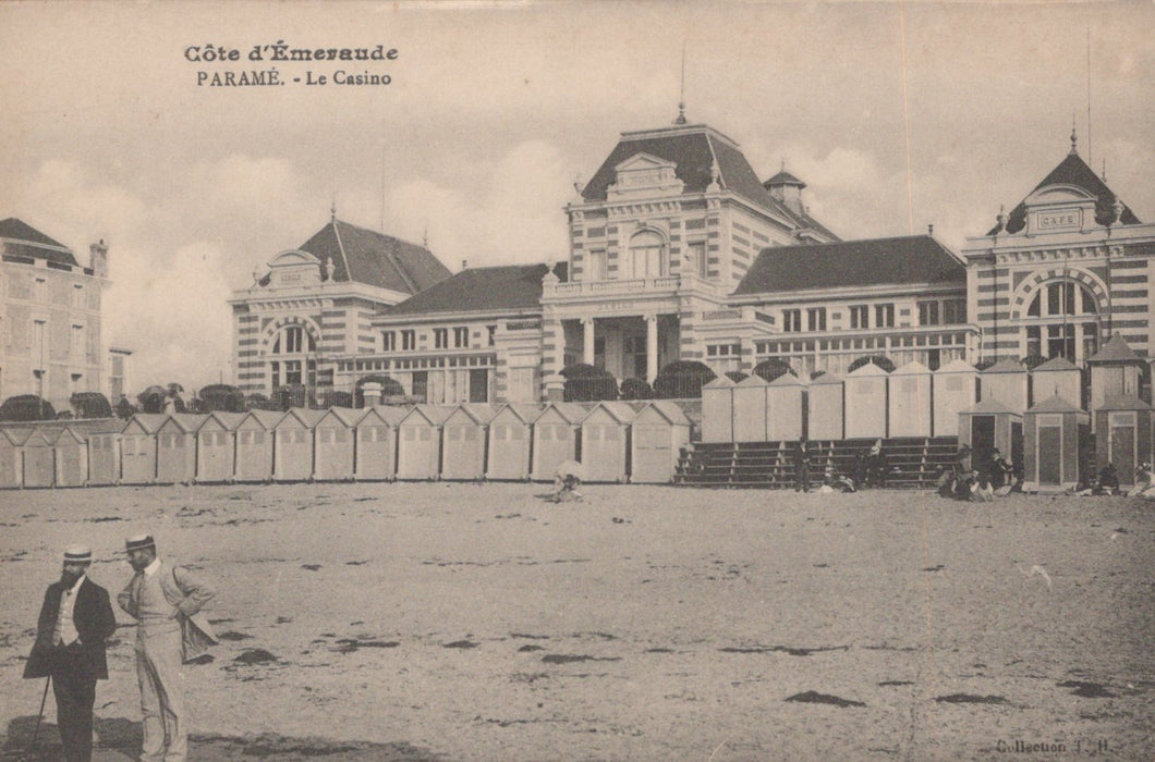 Vintage black and white photo of a coastal scene with buildings and beach huts.