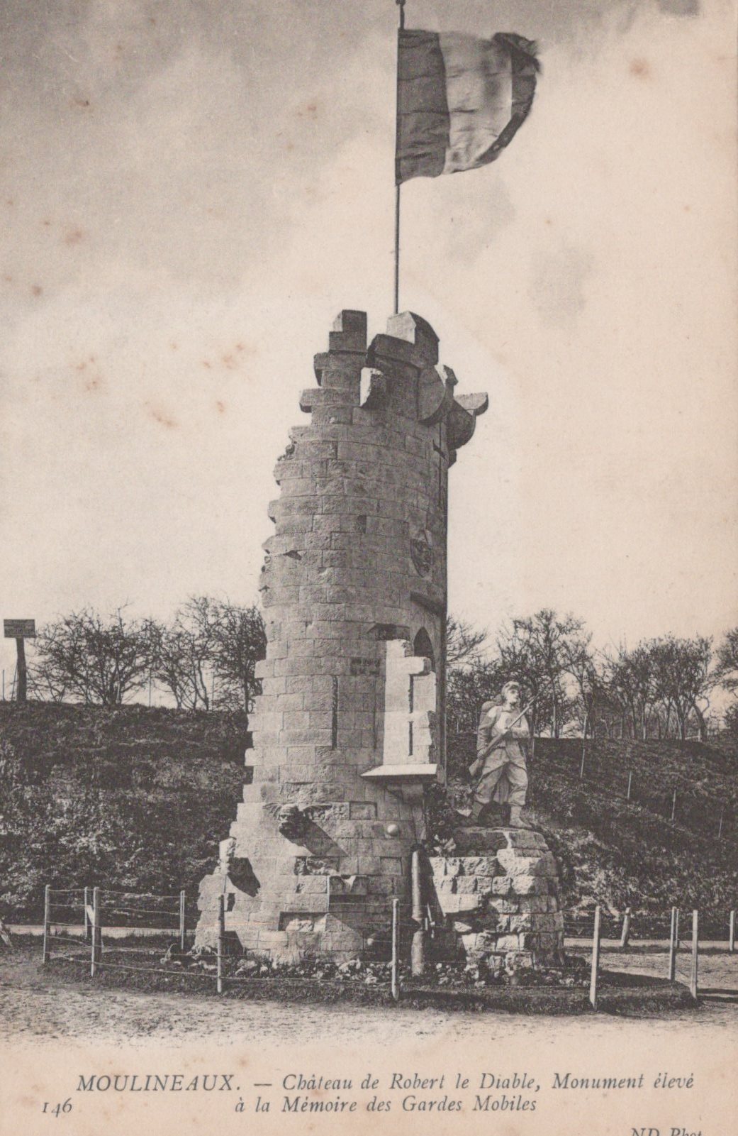 Ruins of a castle with a flag, surrounded by trees and a fence.