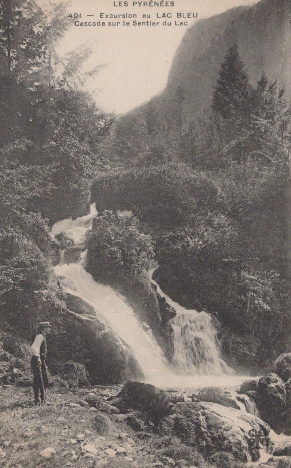 Vintage photograph of a waterfall in a mountainous area with a person standing nearby.