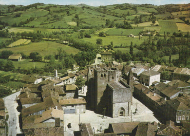 Aerial view of a town with a prominent church in the center, surrounded by green fields.