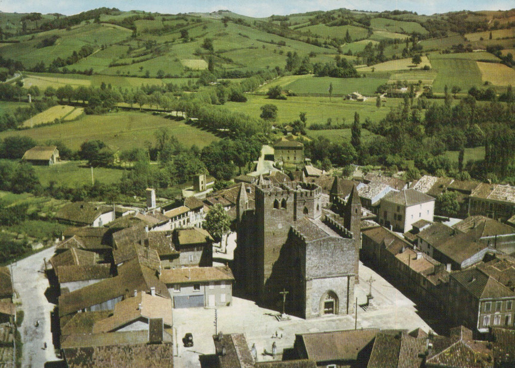 Aerial view of a town with a prominent church in the center, surrounded by green fields.