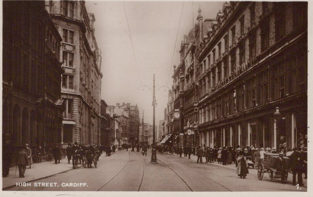 Vintage photograph of a busy street scene in Cardiff, featuring people and horse-drawn carriages.