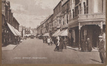 Load image into Gallery viewer, Vintage black and white photograph of a street scene in Porthcawl, featuring people and shops.
