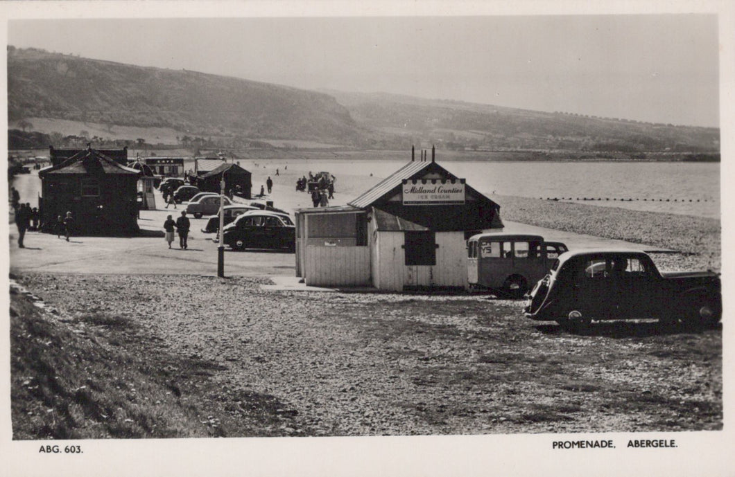 Vintage black and white photo of a beach promenade with huts and cars, featuring 'National Caravan' branding.