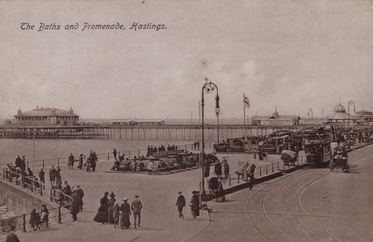 Vintage black and white photo of a promenade with people and vehicles, featuring text 'The Baths and Promenade, Hastings'.