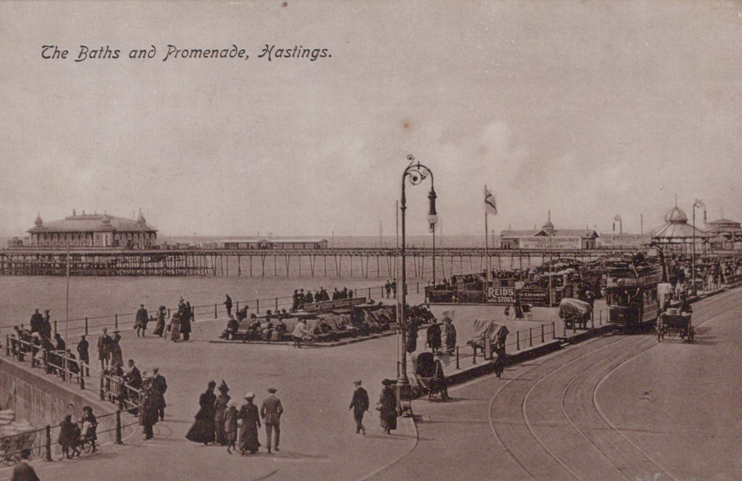 Vintage black and white photo of a promenade with people and vehicles, featuring text 'The Baths and Promenade, Hastings'.