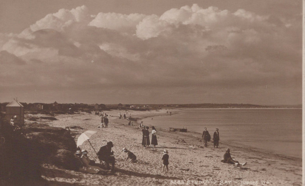 Vintage sepia-toned photograph of a beach scene with people and umbrellas under a cloudy sky.