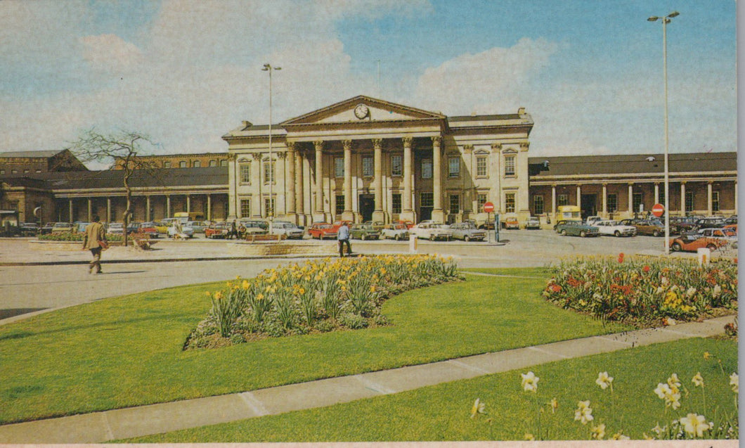 Historic building with a large lawn and flower bed in front, vintage cars parked around.