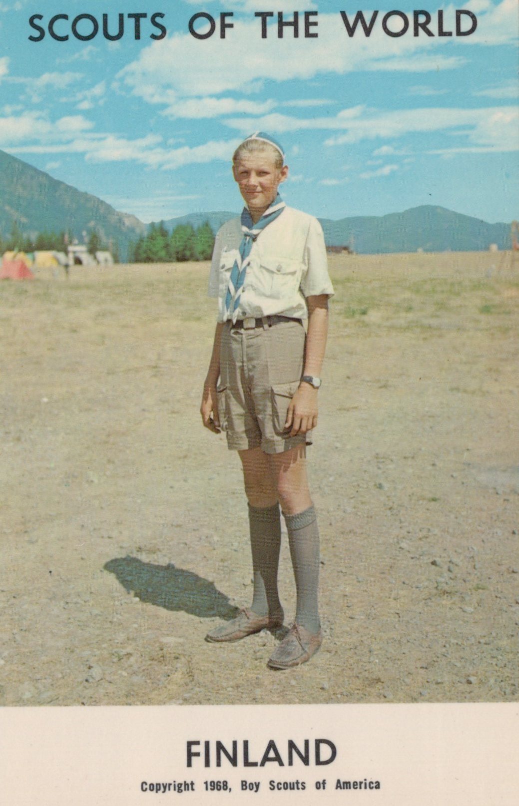 Scout in uniform standing in a field with mountains in the background, labeled 'Scouts of the World, Finland'.
