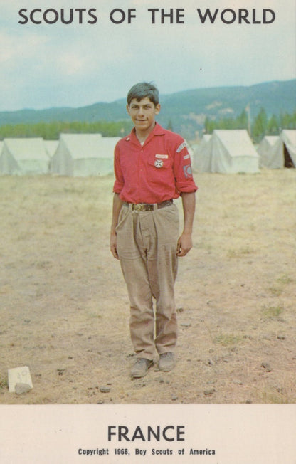 Boy Scout in a red shirt standing in front of tents with 'Scouts of the World' text at the top.