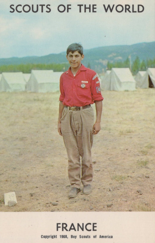 Boy Scout in a red shirt standing in front of tents with 'Scouts of the World' text at the top.