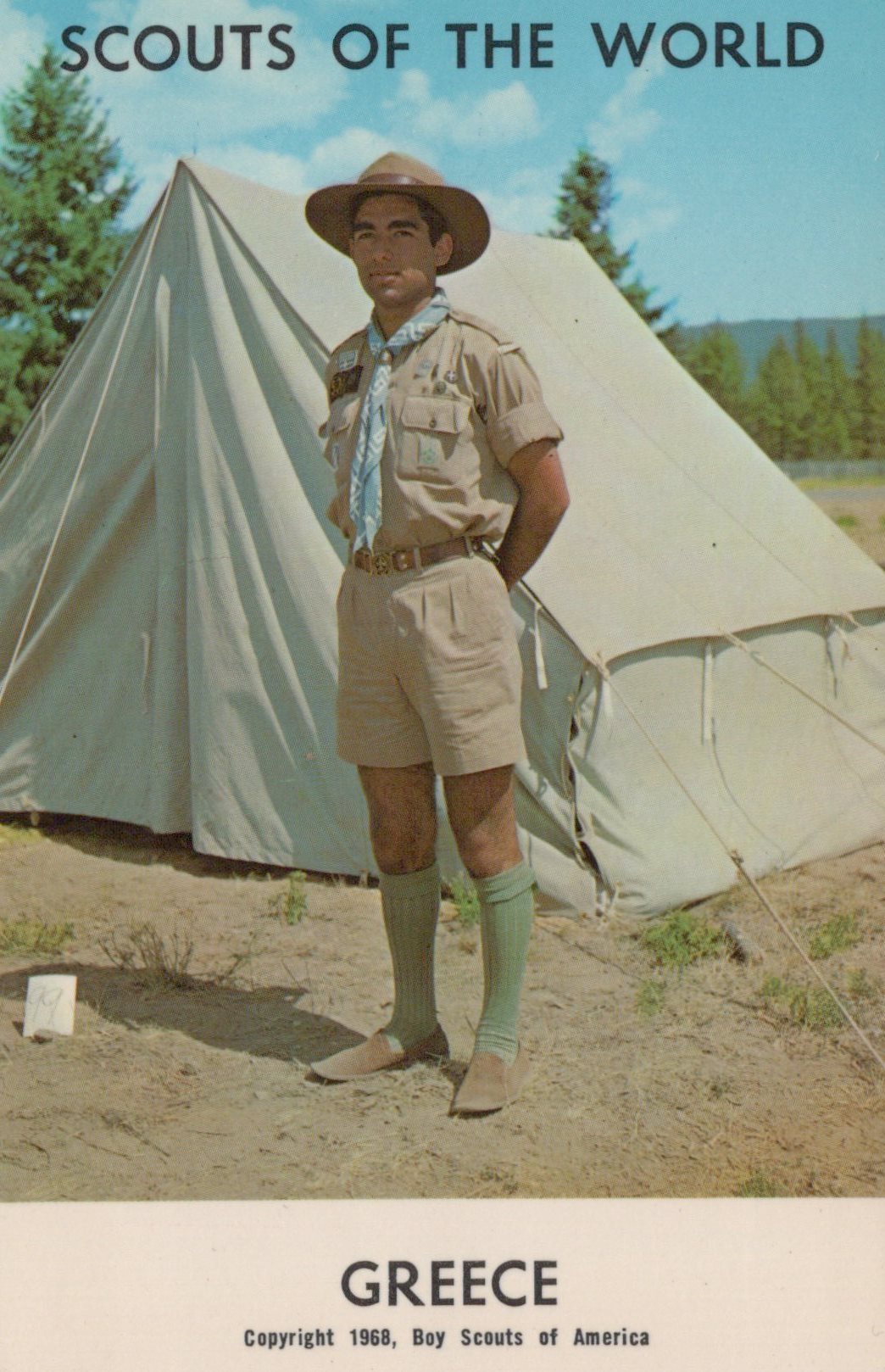 Scout standing in front of a tent with 'Scouts of the World' and 'Greece' text.